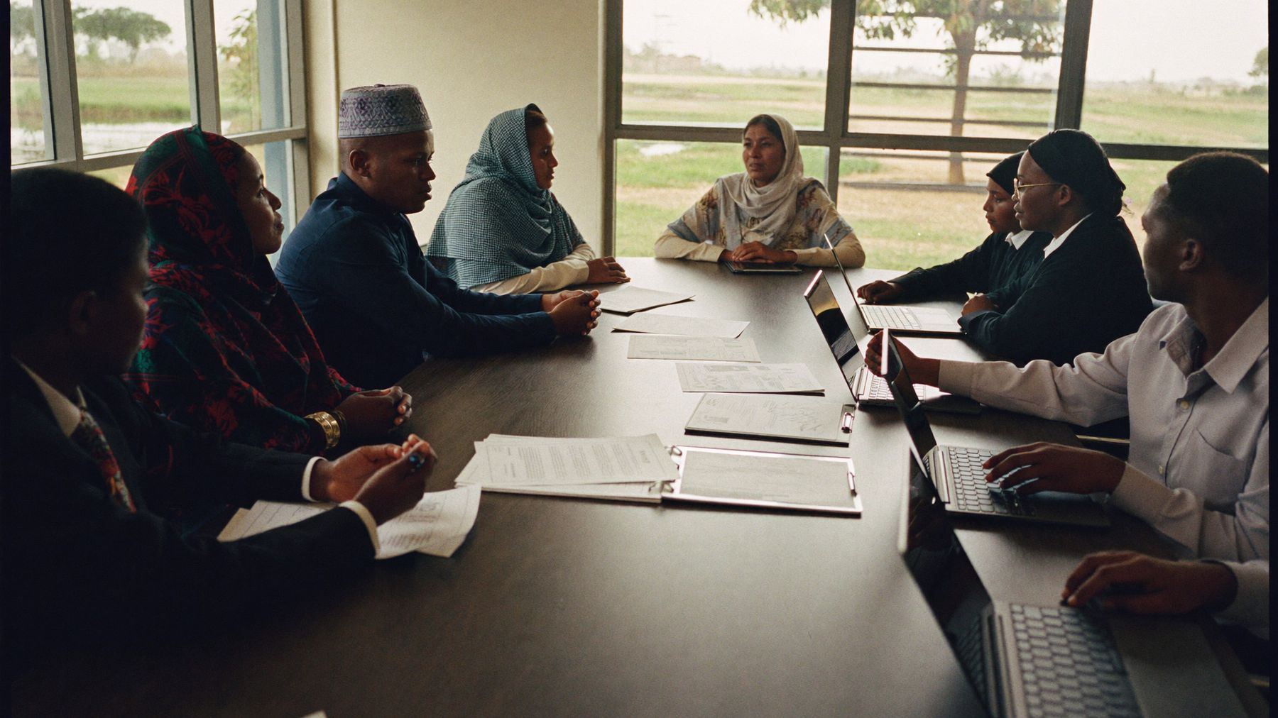 A professional meeting around a boardroom table with Somali women and men, laptops and printed documents in front of them.