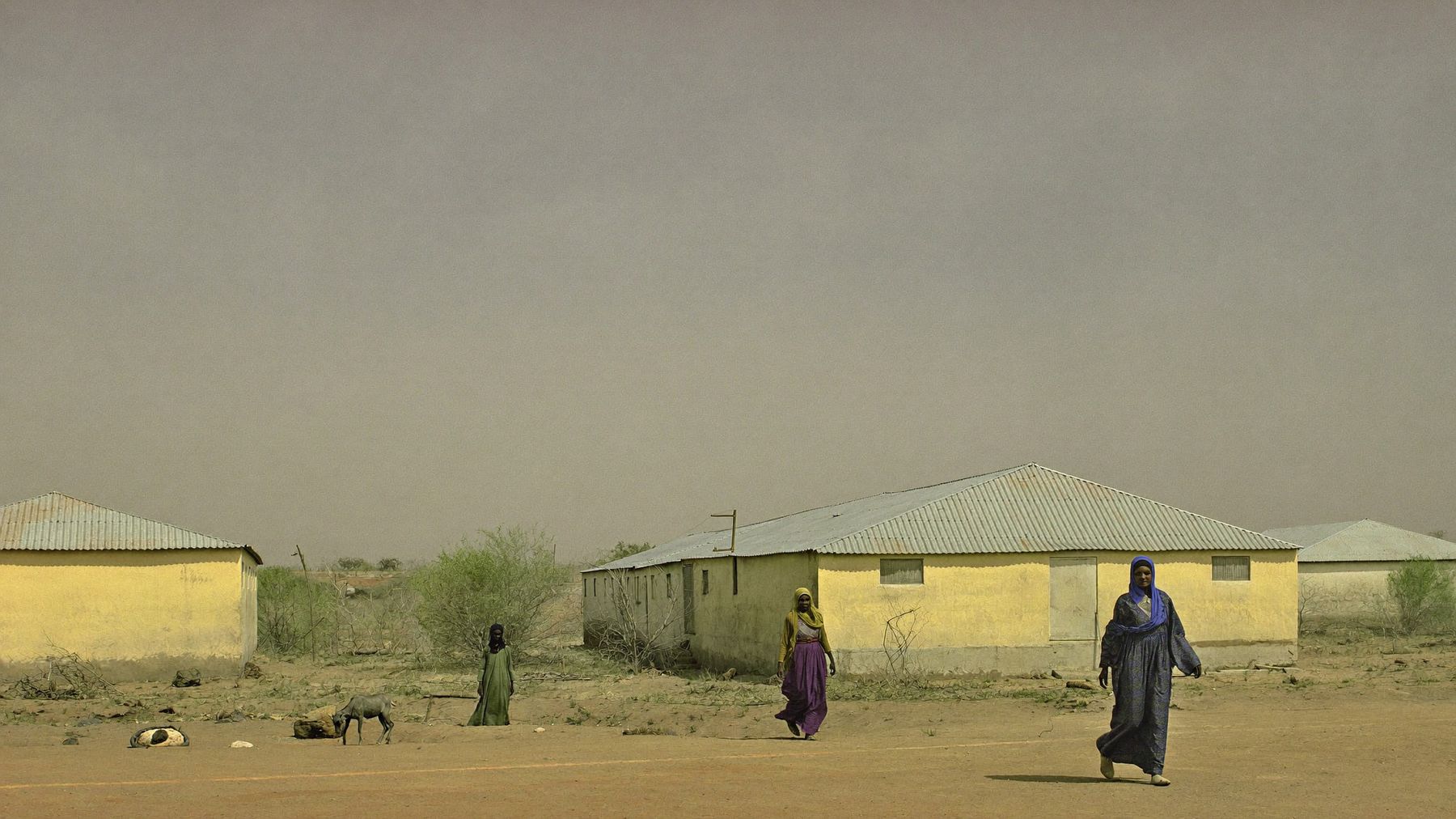 An inland Somali town in mid-morning light, with women trading at open shopfronts along a broad sandy street.