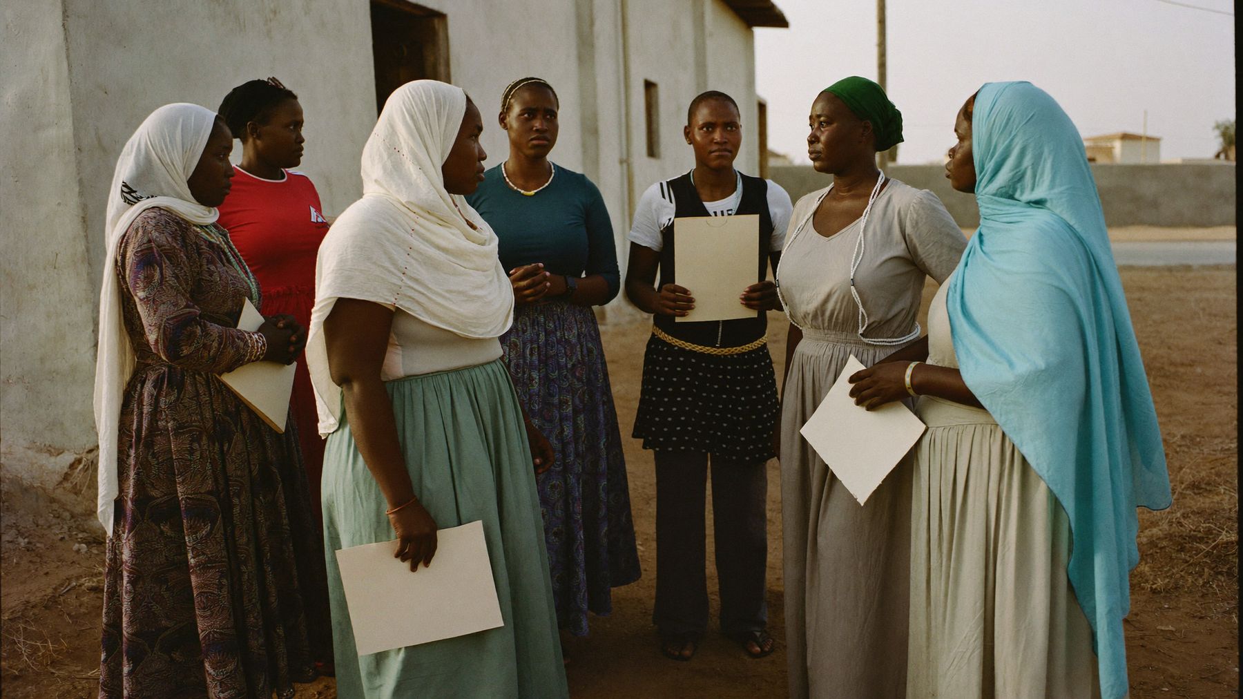 Somali women stand together outside a cooperative building after a producer group meeting, several holding notebooks.