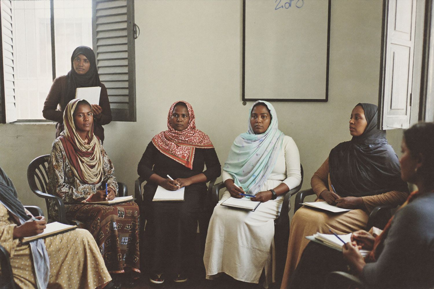 Somali women seated in a semicircle during a women's group planning session in a bright meeting room.