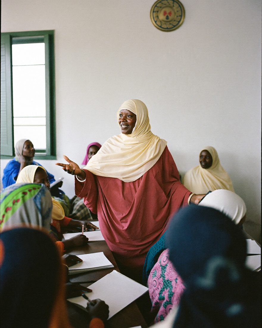 A Somali woman stands and addresses a meeting of women seated with notebooks.